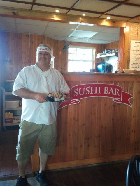 Chef Don standing by the Sushi Bar sign